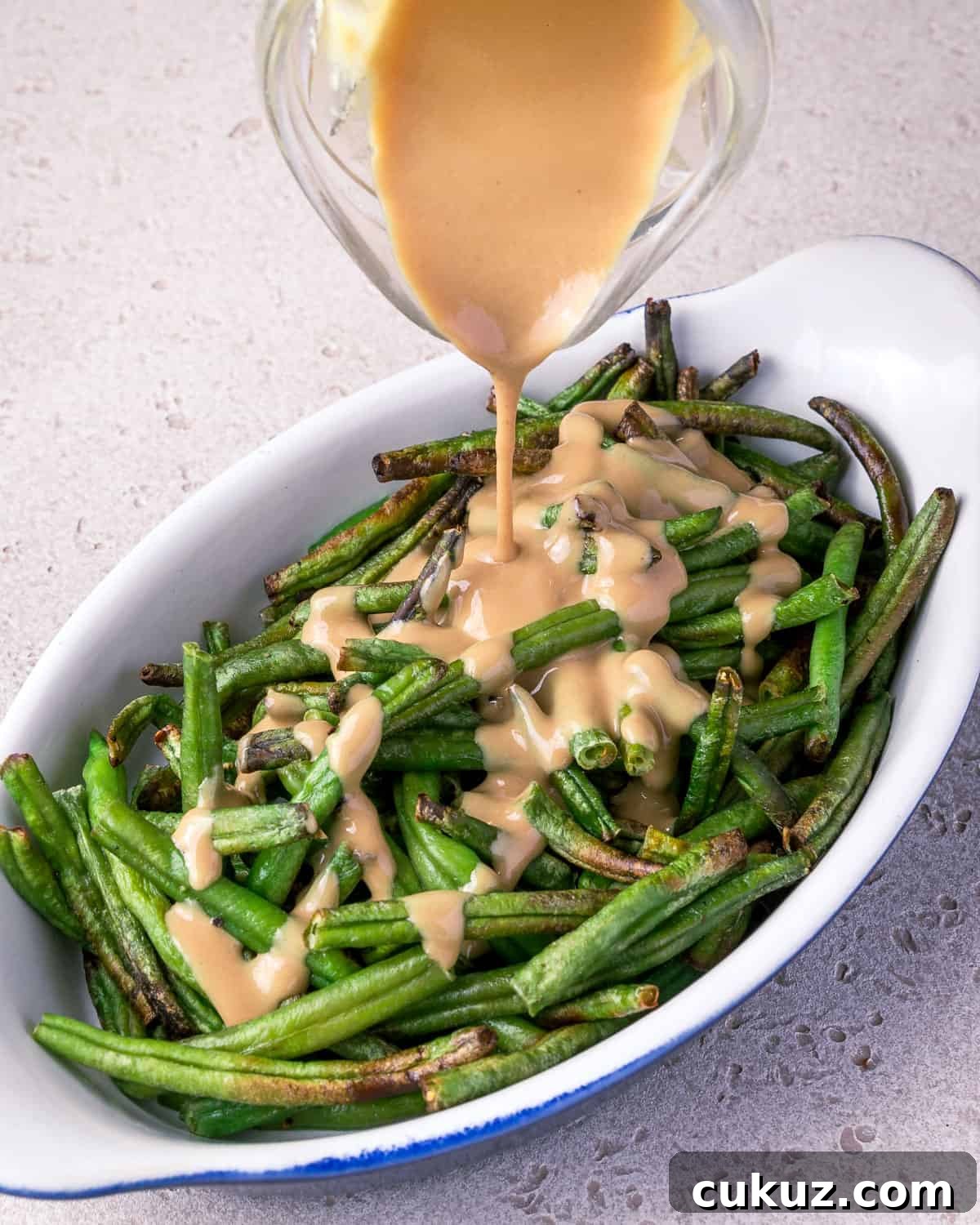 Photo showing tahini sauce being poured on top of a dish of air fried frozen green beans.