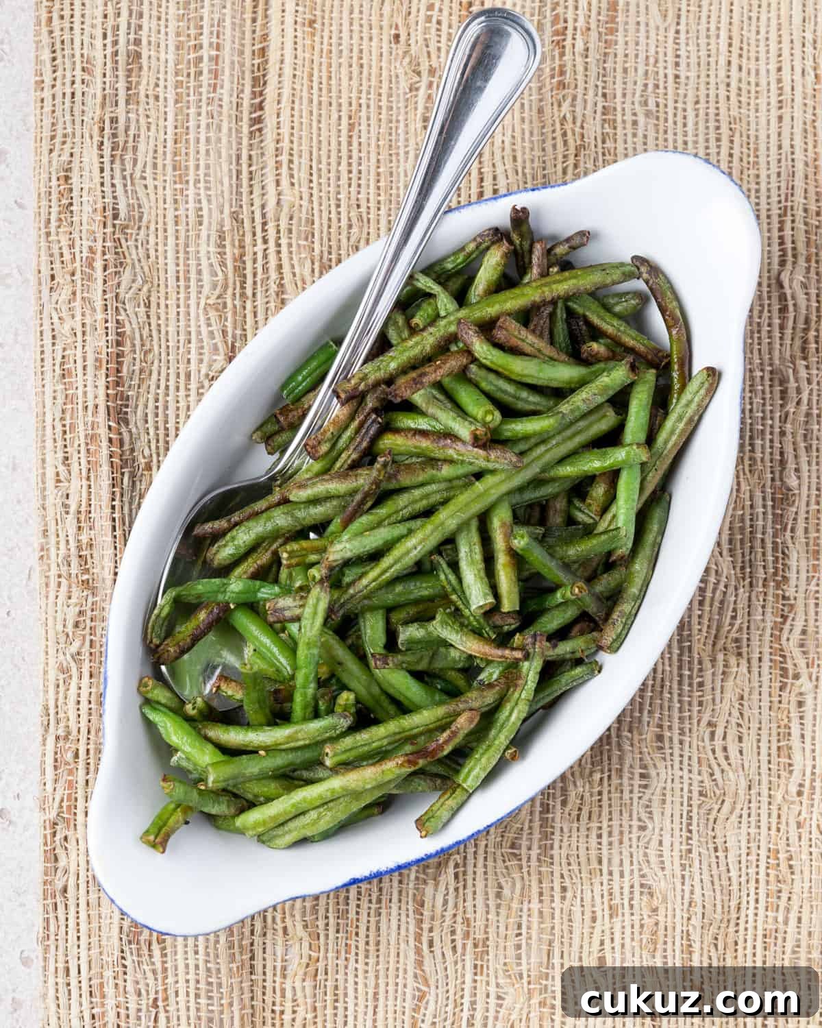 Overhead photo showing a dish of air fried frozen green beans with a spoon ready for serving.