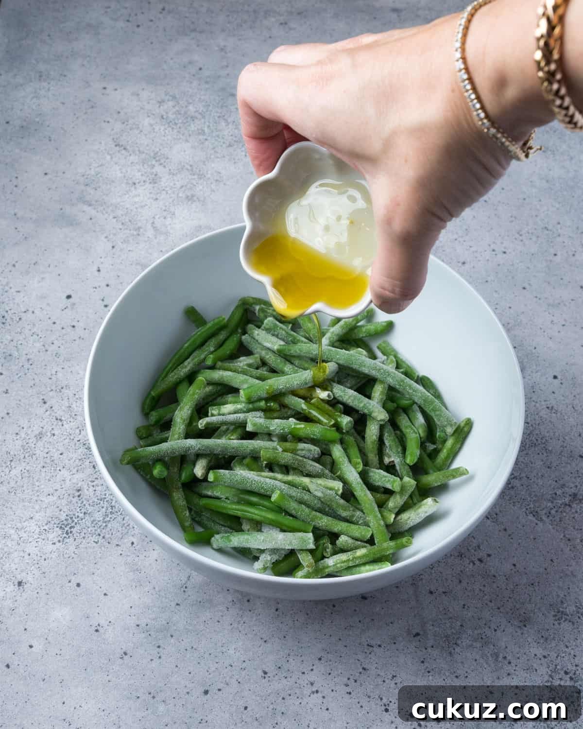 Photo showing olive oil being poured onto a bowl of frozen green beans.