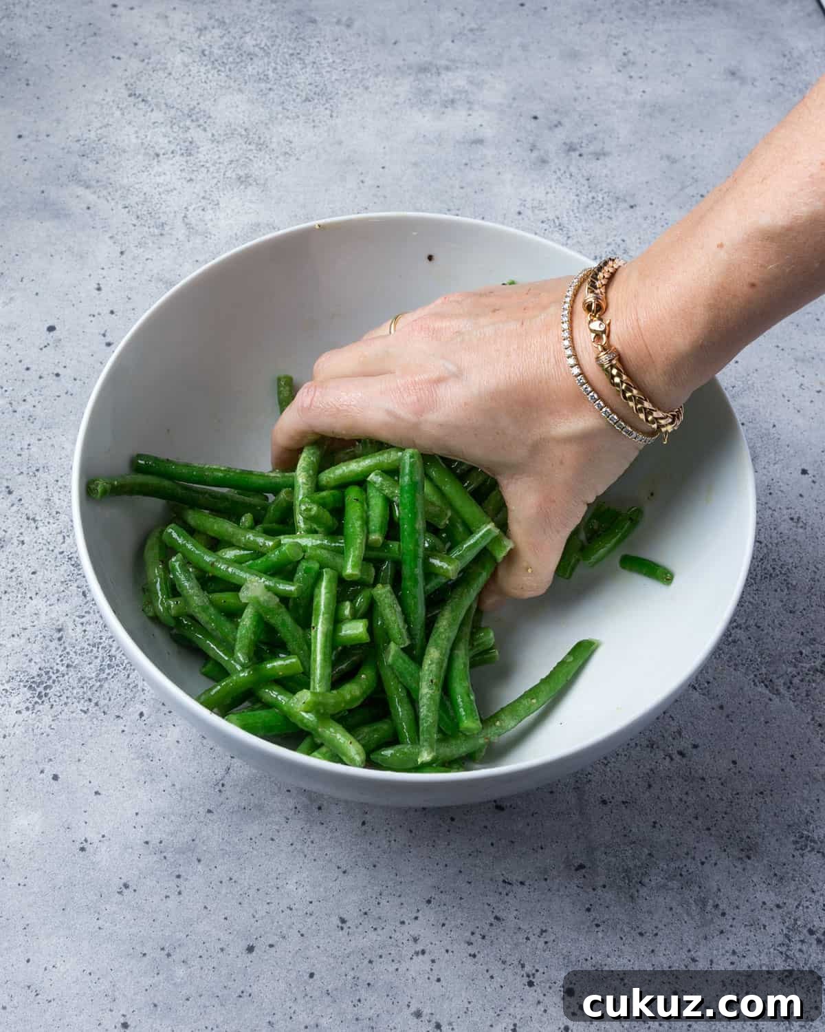 Photo showing green beans being mixed with the oil and seasonings in a bowl.