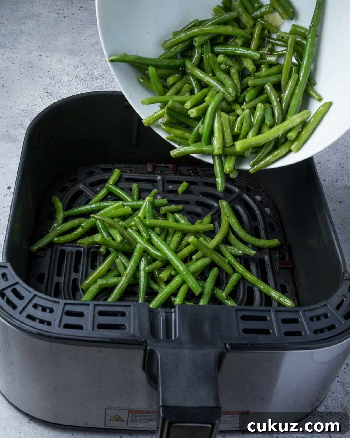 Photo showing seasoned green beans being added to the air fryer.