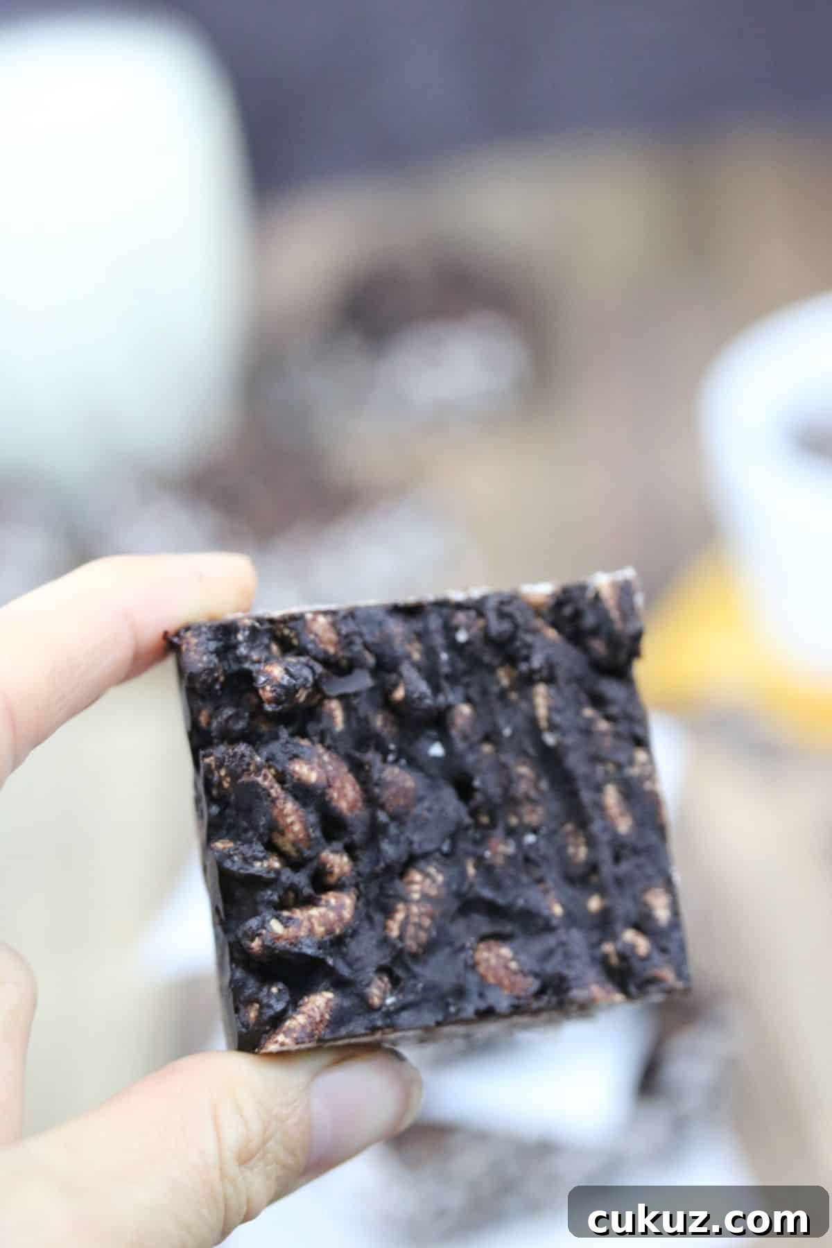 Two fingers holding up a square of a dark chocolate and peanut butter crunch bar.