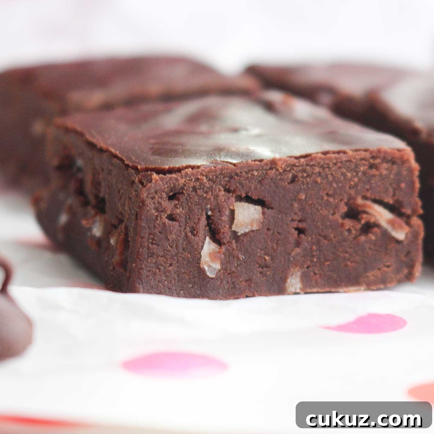 Closeup side view of one square of chocolate fudge with other squares in the background.