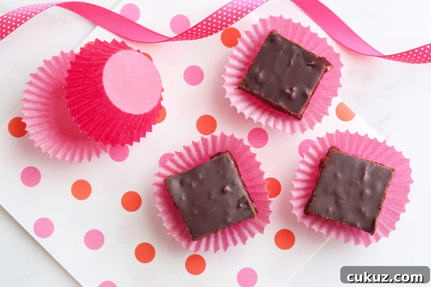 Three little squares of fudge in cupcake papers on a decorative background.