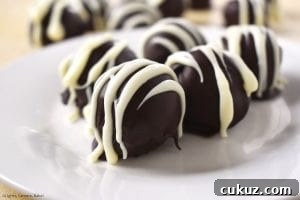 No-Bake Chocolate-Dipped Oreo Truffles 2 Close up of the Oreo Truffles on a plate with other truffles in the background. Covered in melted chocolate and drizzled with melted white chocolate for the professional and indulgent finish.