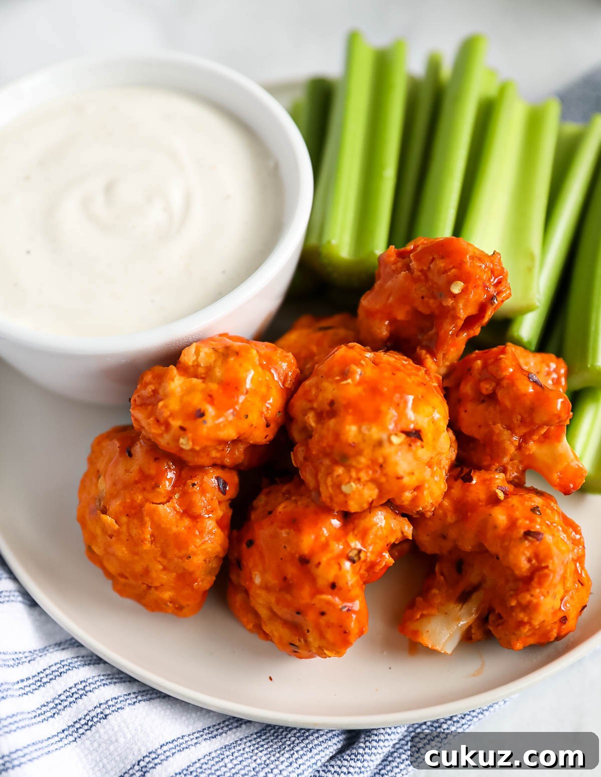 A close-up picture of buffalo cauliflower wings on a plate with a dish of ranch dressing and celery