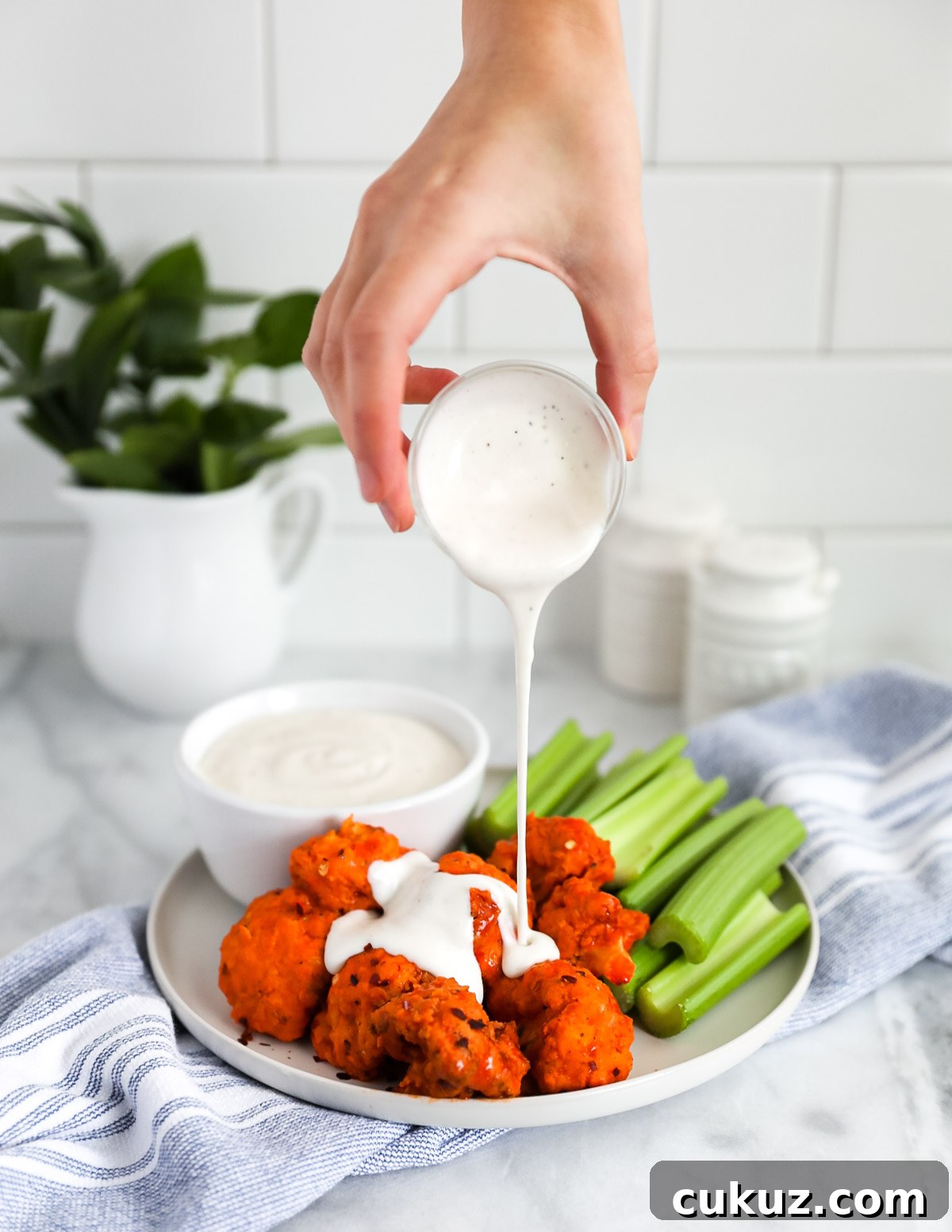 A hand pouring a drizzle of ranch dressing on a plate of cauliflower wings.