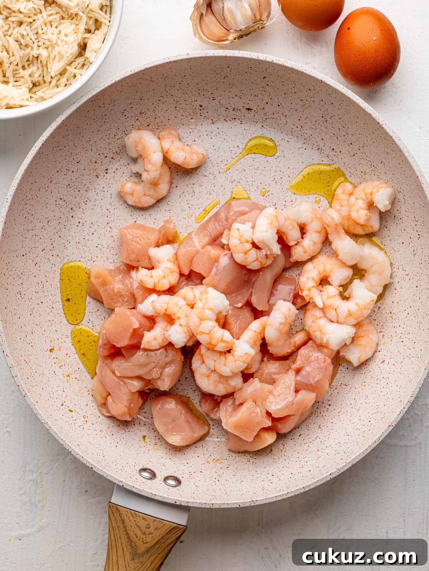 Uncooked chicken and shrimp in a frying pan.