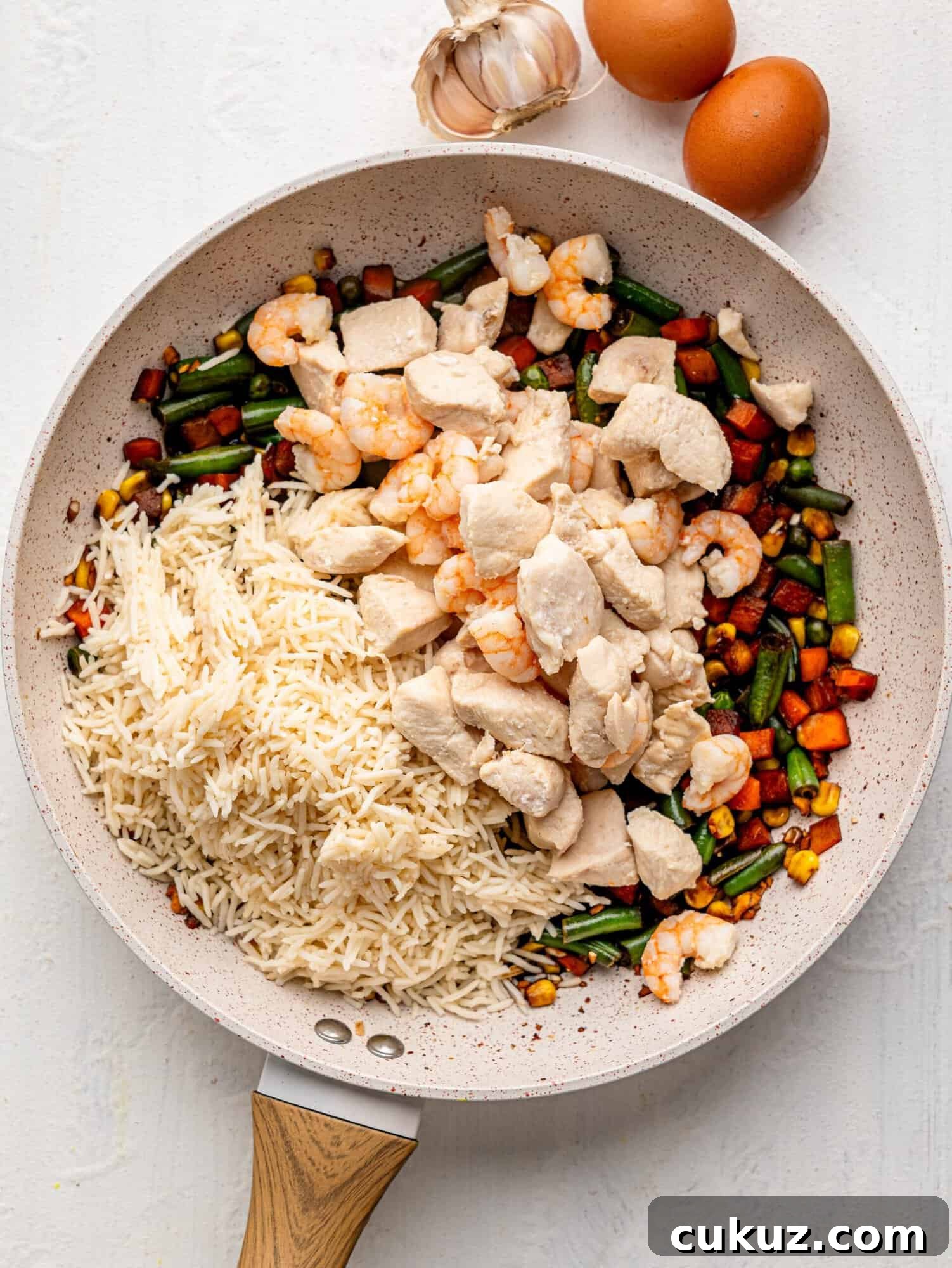 Mixed vegetables, soya sauce, cooked rice, chicken and shrimp in a frying pan.