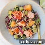 The salmon mango salad in two bowls with a fork. Lime wedge and sesame seeds are are on the side.
