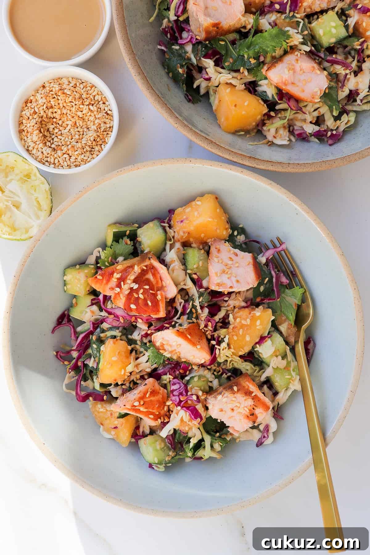 Mango salad bowls shot in the sunlight with a squeezed lime wedge, tahini sauce and toasted sesame seeds in a dish on the side.