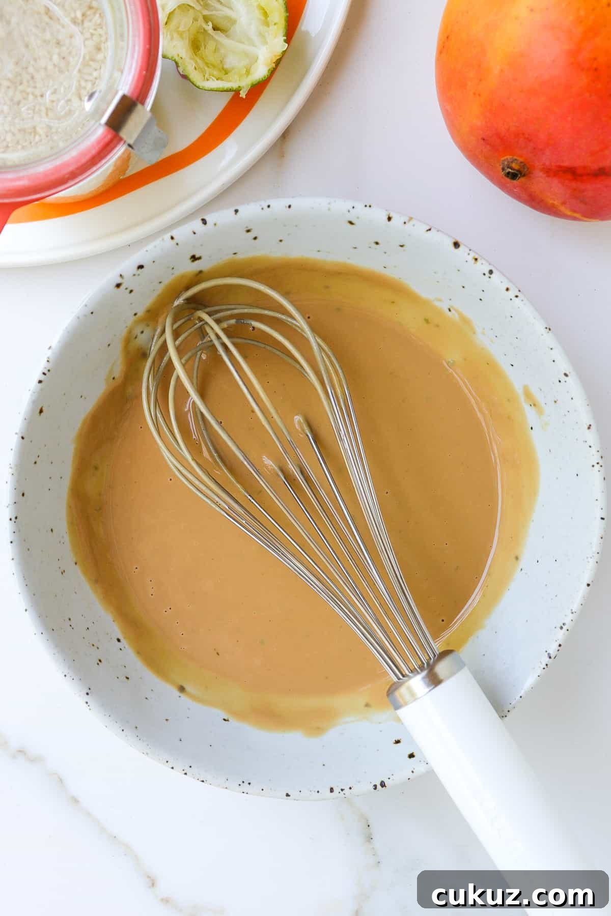 Tahini lime dressing in a bowl with a whisk.