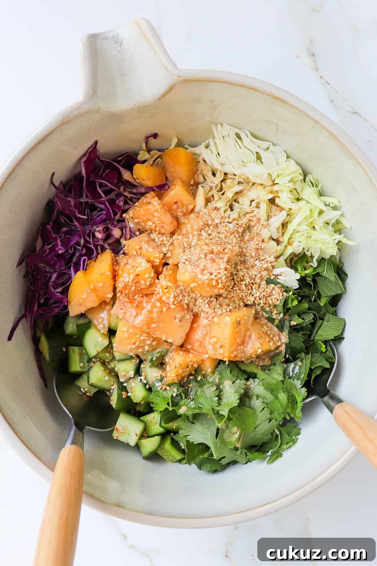 The mango salad in a mixing bowl with wooden spoons.