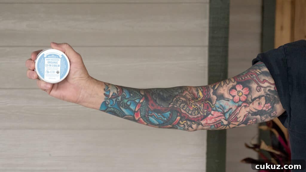 Person with tattoo sleeve holding Dr. Bronner's Unscented Magic Balm - tattoo care