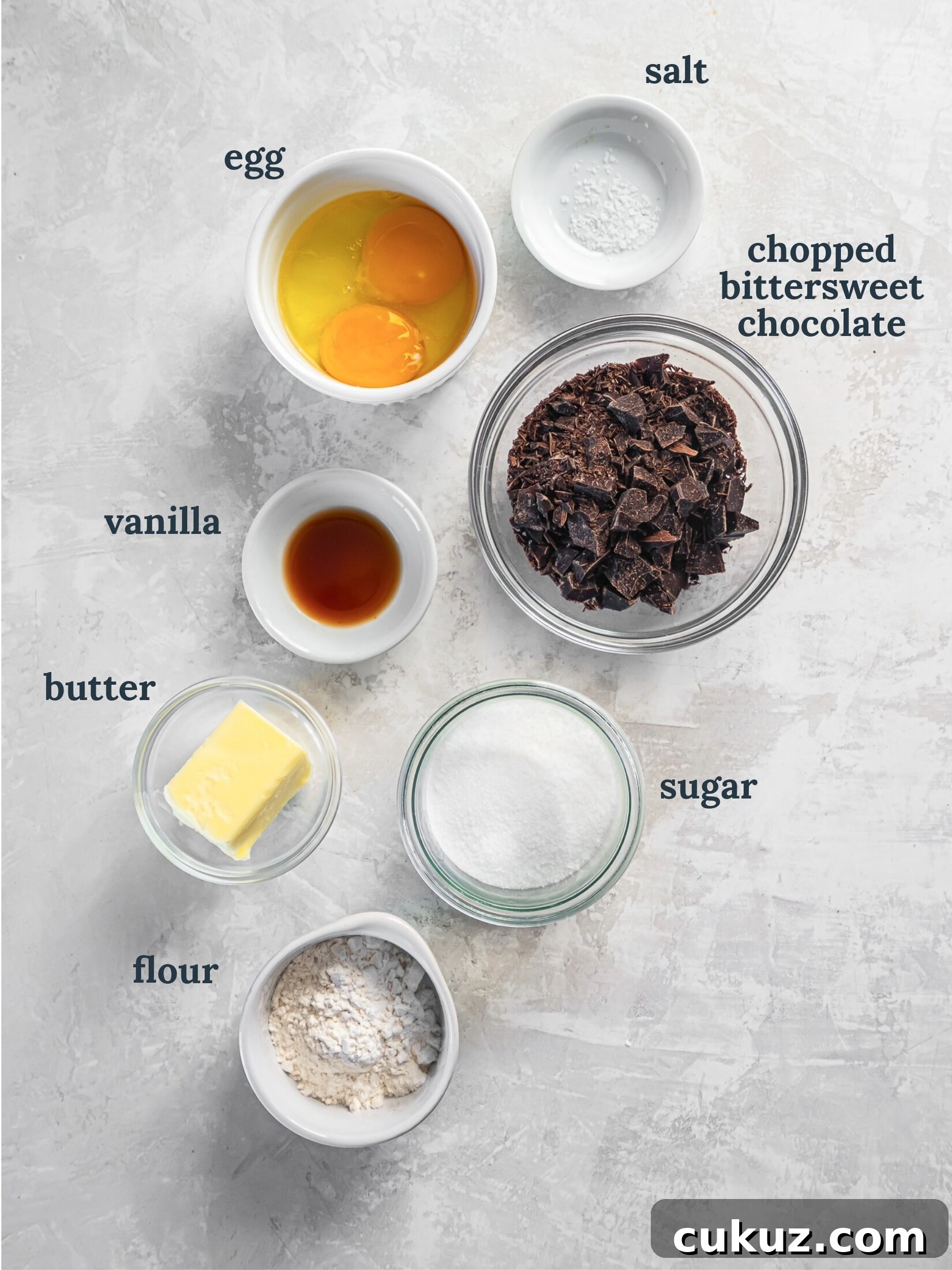 Small bowls with eggs, chocolate, vanilla, sugar, butter and flour.