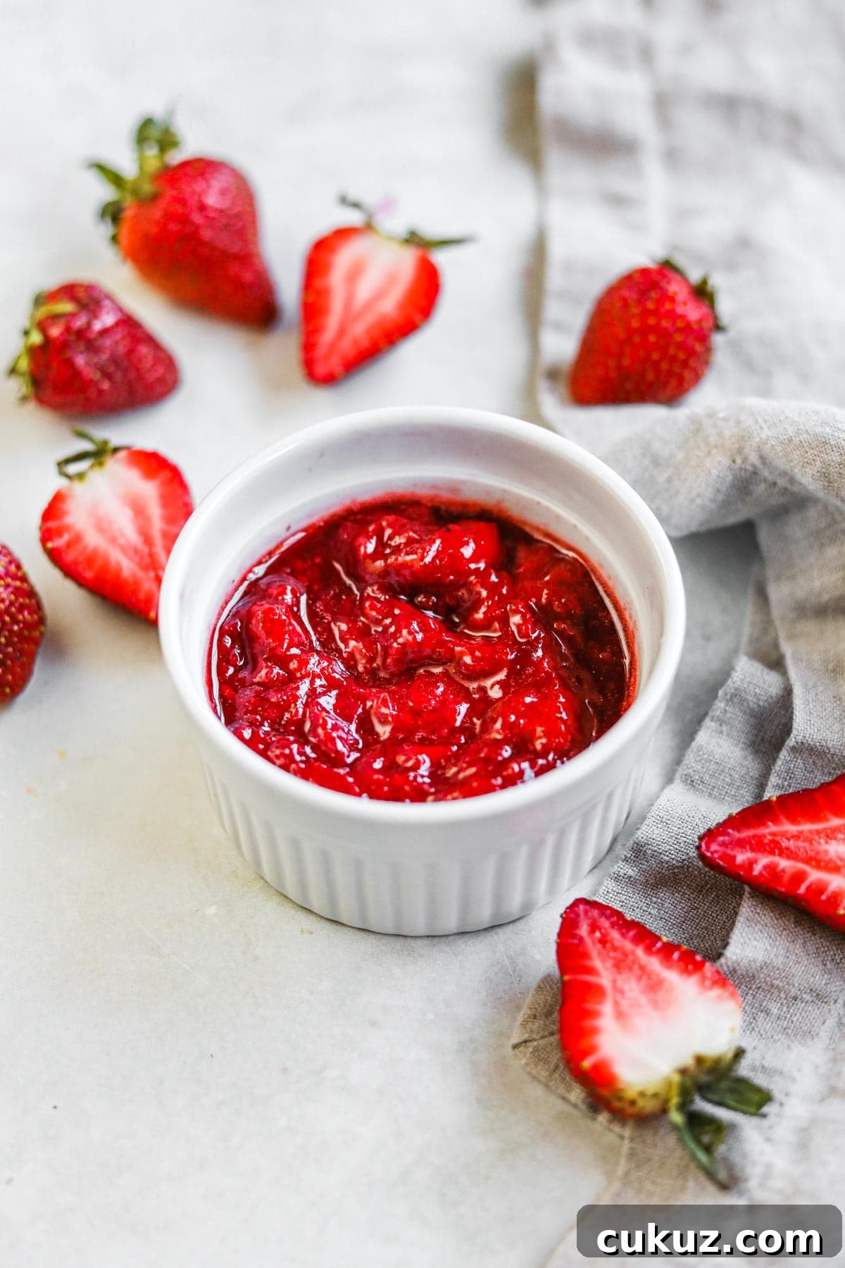 Homemade strawberry compote (for ice cream, yogurt, desserts, and more) in a white ceramic ramekin with cut strawberries.