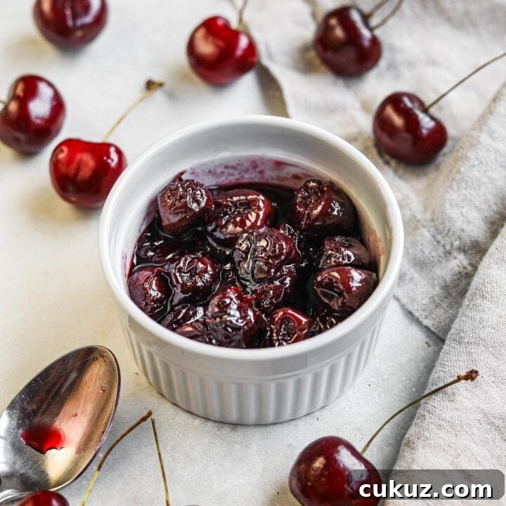 Homemade cherry compote in a white ramekin with cherries and a spoon with cherry syrup.