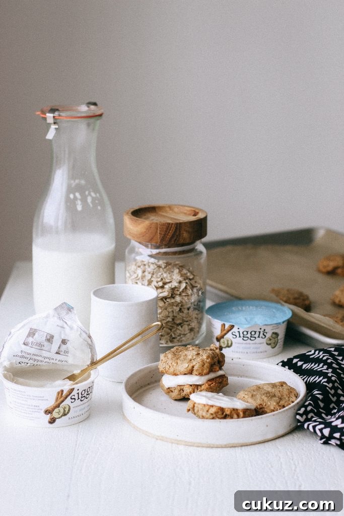 Low-Sugar Gluten-Free Oatmeal Cookie Sandwich with Cinnamon Yogurt Filling 3 Oatmeal cookie sandwiches with yogurt filling on a white plate with jug of milk and yogurt containers
