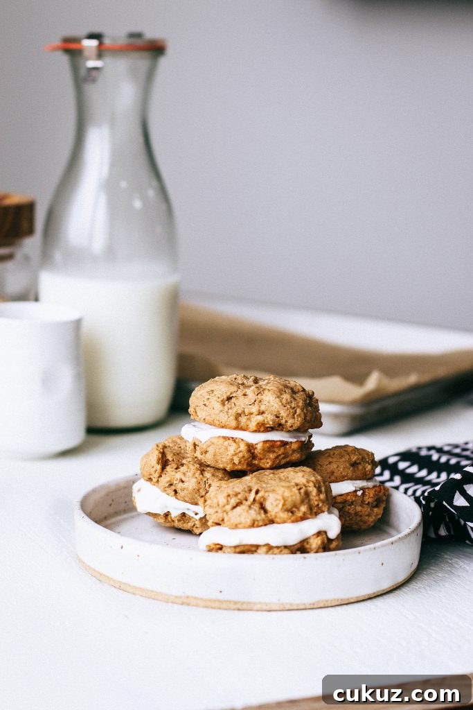 Low-Sugar Gluten-Free Oatmeal Cookie Sandwich with Cinnamon Yogurt Filling 4 oatmeal yogurt cookie sandwiches stacked on plate with jar of milk