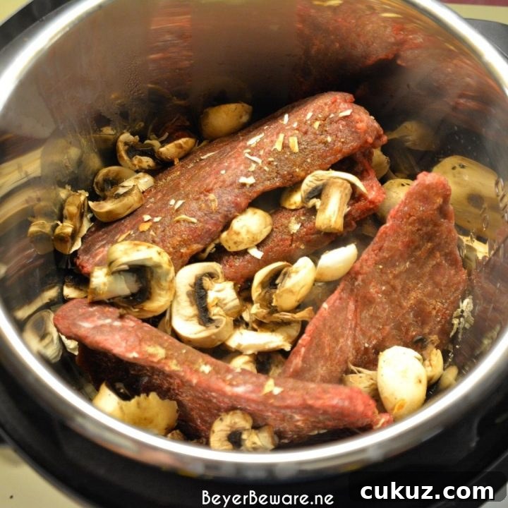 Layered cubed steaks, mushrooms, and soup mix ready for the Instant Pot.