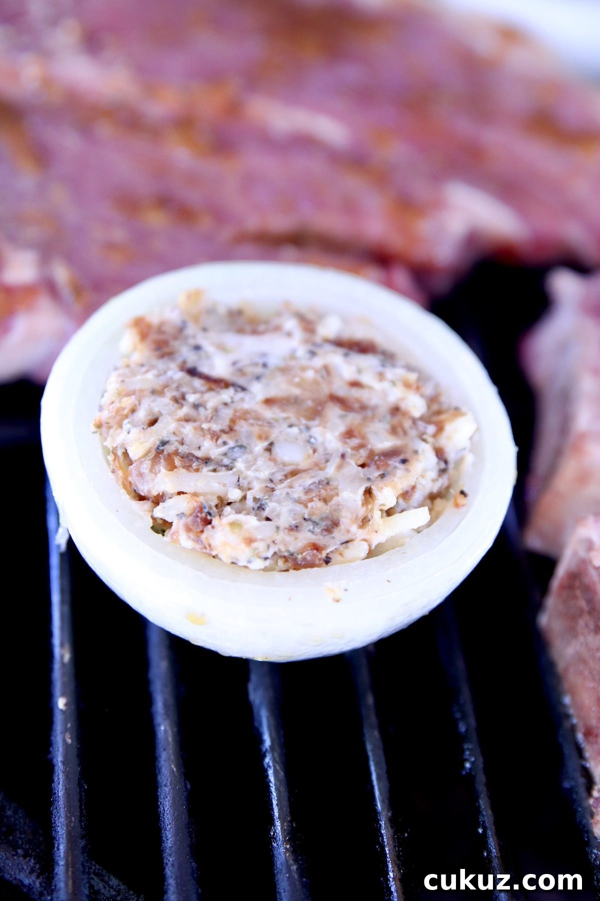 stuffed onions recipe with cheese, caramelized onions and herbs stuffed onion on a grill - steak in background