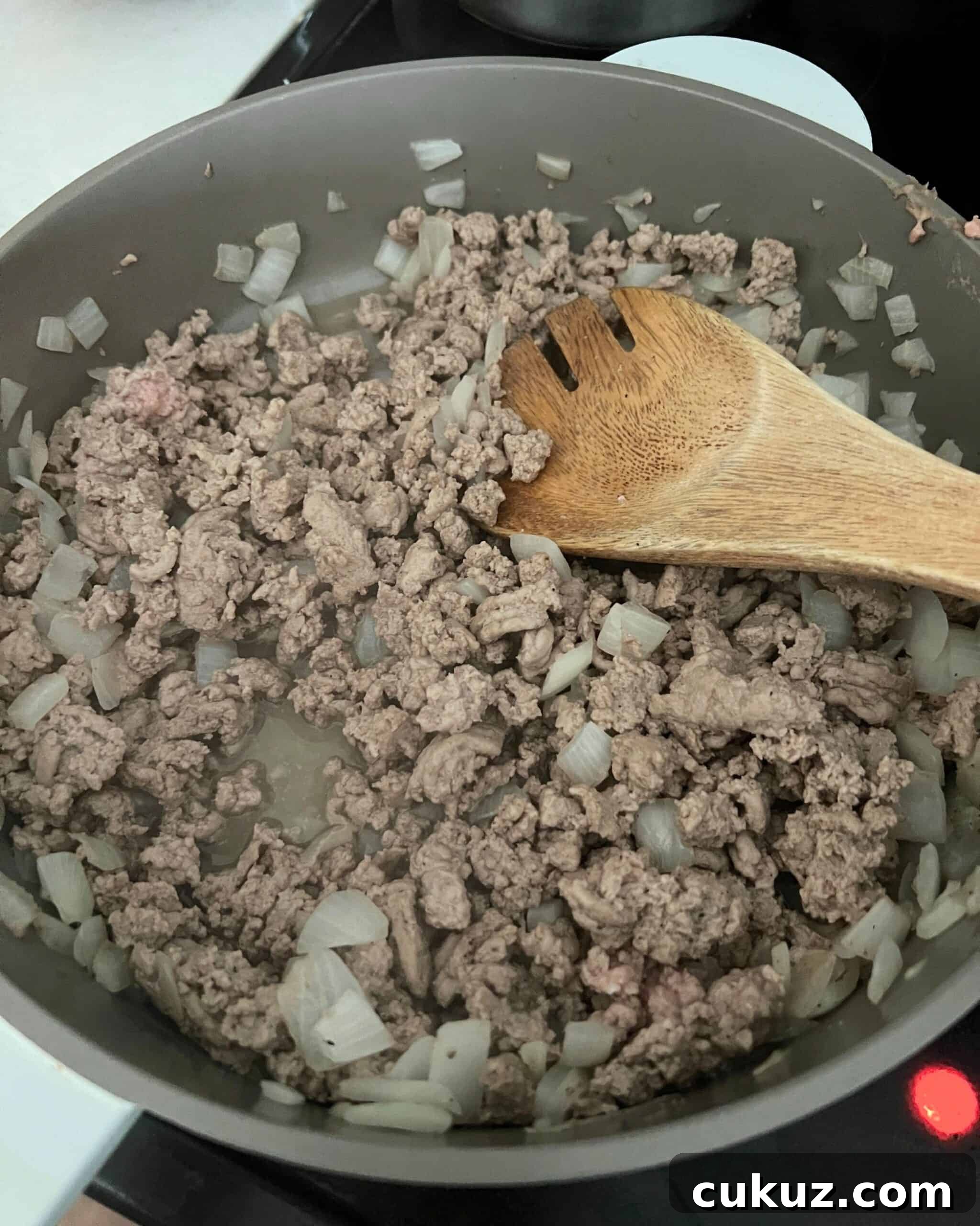 Ground turkey and onions cooking in a skillet with a wooden spoon. 