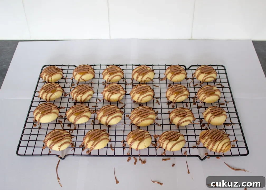 Twix thumbprint cookies with drizzled chocolate on a wire rack