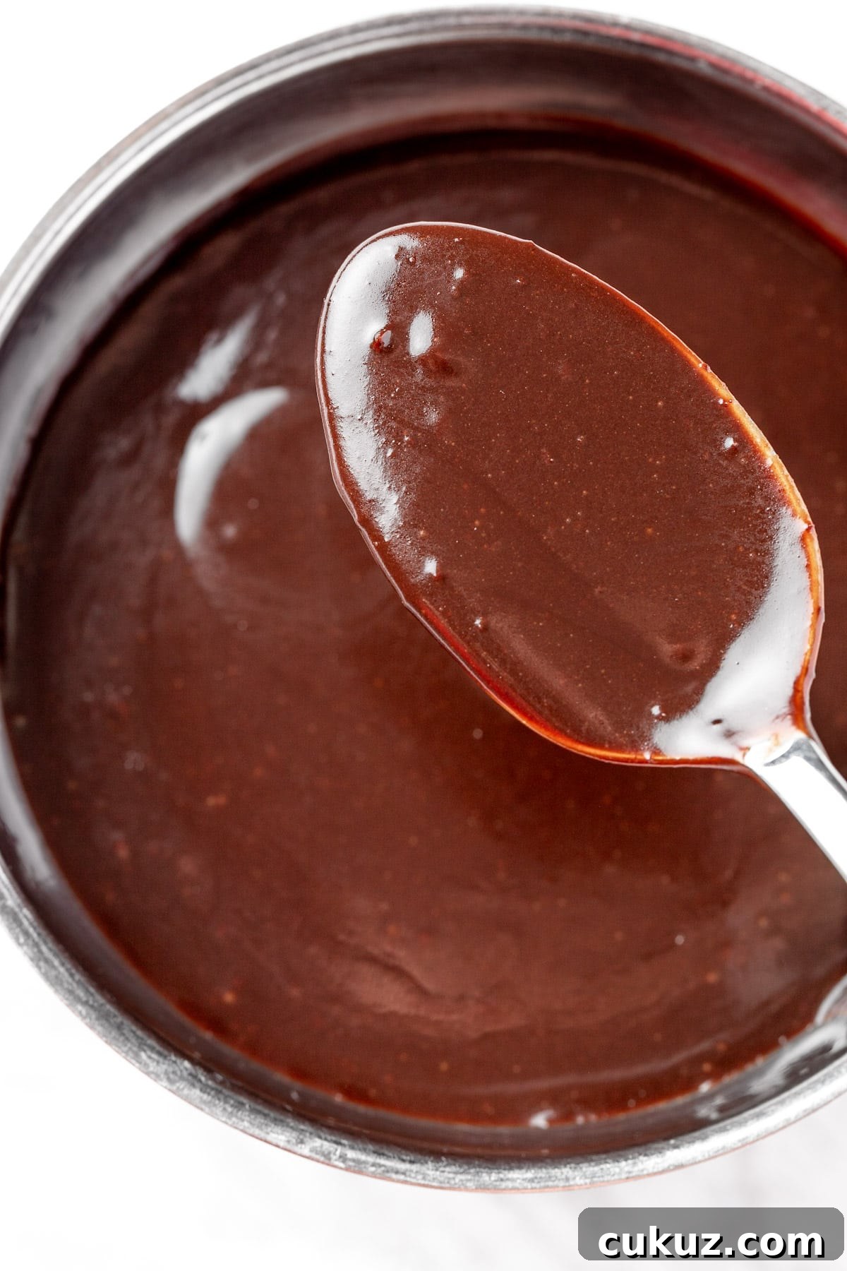 A spoonful of chocolate pancake syrup held over a bowl of the chocolate sauce.