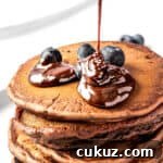 Chocolate pancake syrup being drizzled on top of a stack of pancakes.