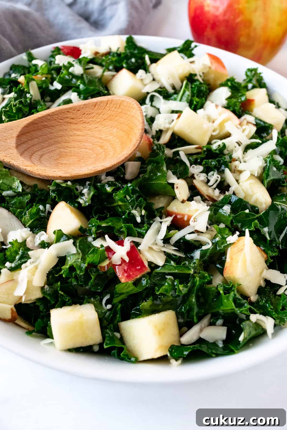 Kale Salad with Apples and Cheddar with a wooden serving spoon.