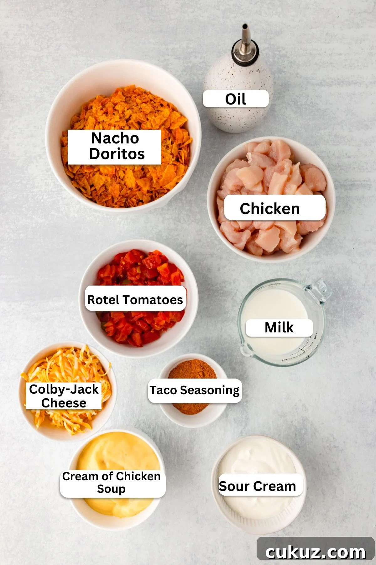 Top view of nine bowls on a light surface. Bowls contain labeled ingredients: Nacho Doritos, chicken pieces, oil, Rotel tomatoes, milk, Colby-Jack cheese, taco seasoning, cream of chicken soup, and sour cream.