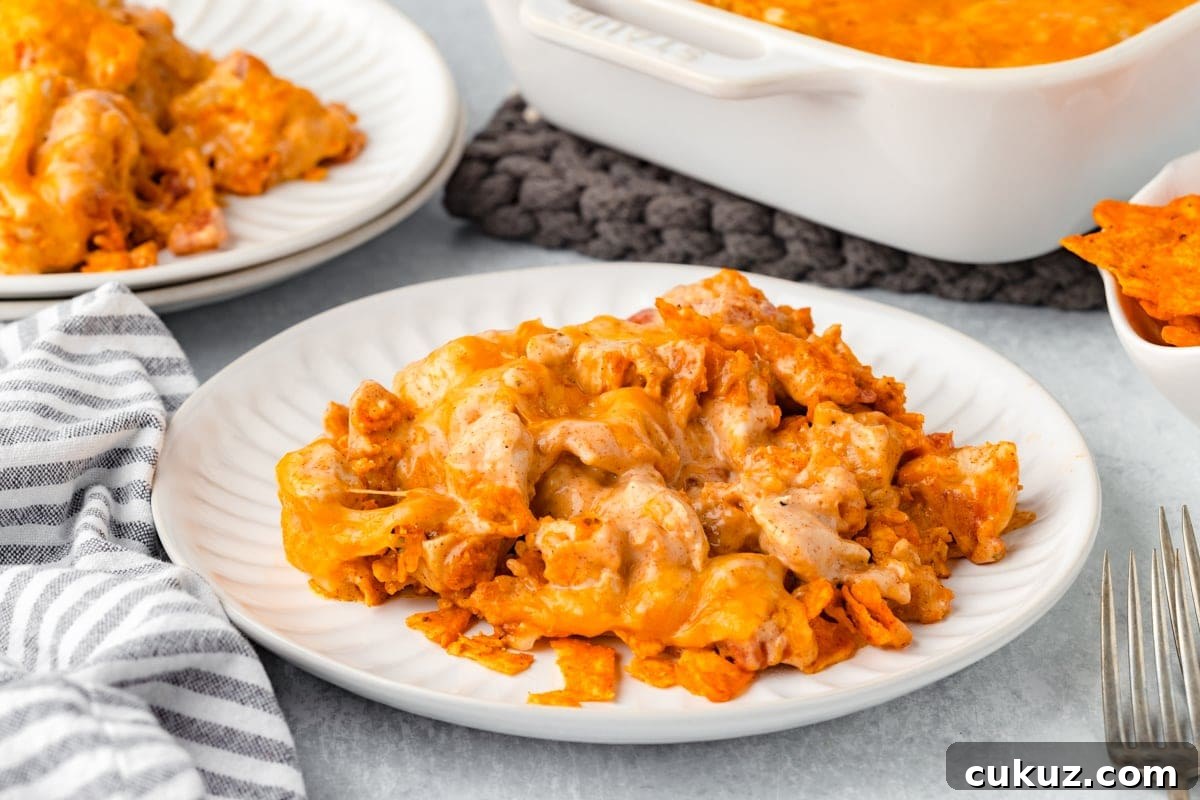 A plate of cheesy nacho casserole sits on a white table. The dish is topped with melted cheese and nacho chips. A napkin, forks, and casserole dish are nearby, creating a cozy dining setting.