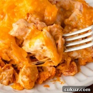 A fork digging into a cheesy Doritos casserole on a white plate.