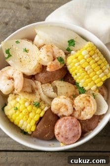 a bowl filled with shrimp, potatoes, onions, smoked sausage, and corn and sprinkled with old bay seasoning