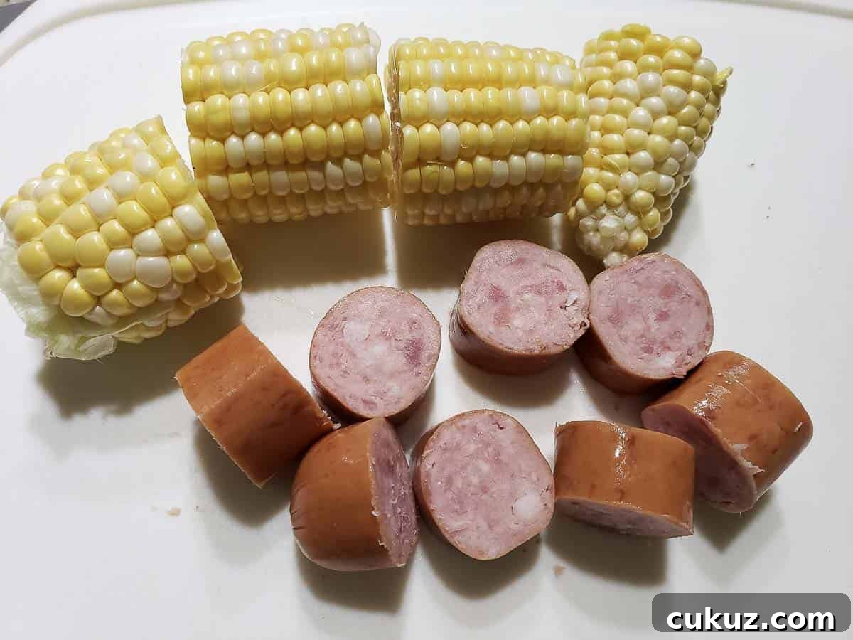 a corn on the cob cut into 4 pieces and diced smoked sausage on a cutting board.