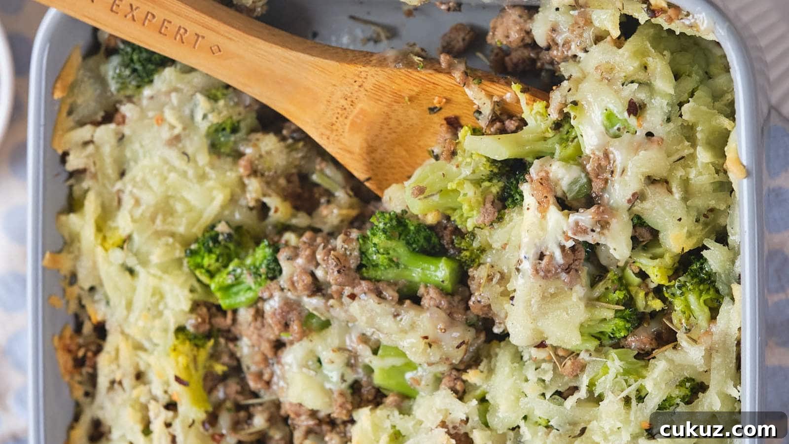 A baked casserole dish with ground beef and broccoli casserole and a wooden spoon.