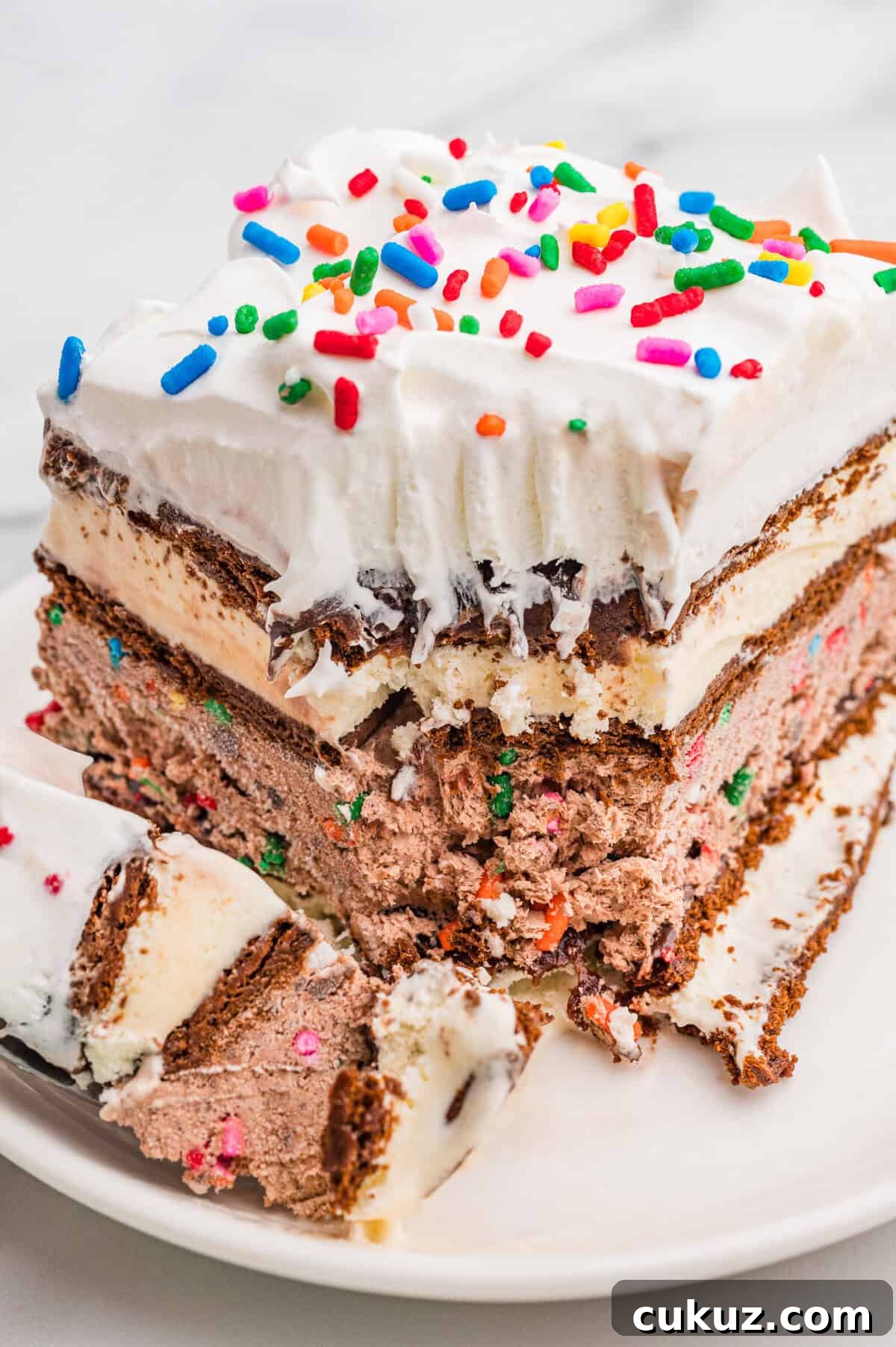 Partially eaten slice of ice cream sandwich cake with whipped topping and sprinkles.