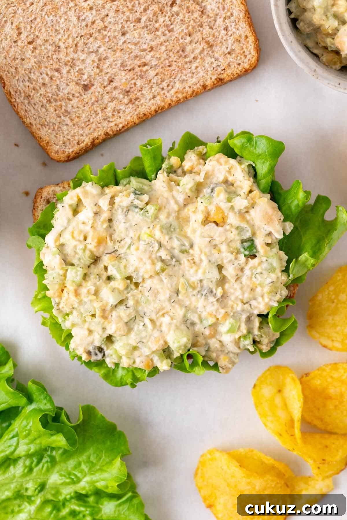 Vegan chickpea salad sandwich open-faced with lettuce and served with potato chips