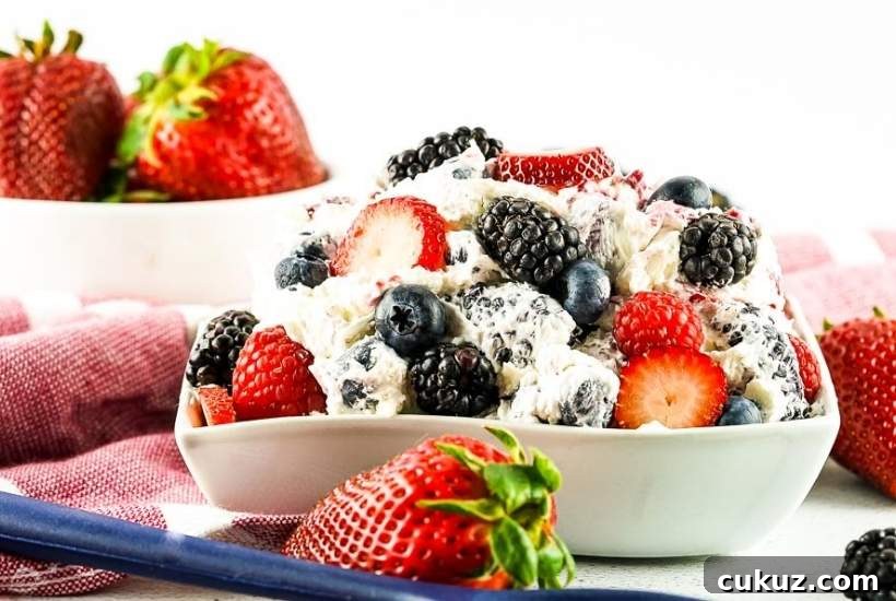 Summer Berry Cheesecake Salad Recipe with Creamy Whipped Topping 7 red, white, and blue cheesecake salad in a bowl next to whole strawberries