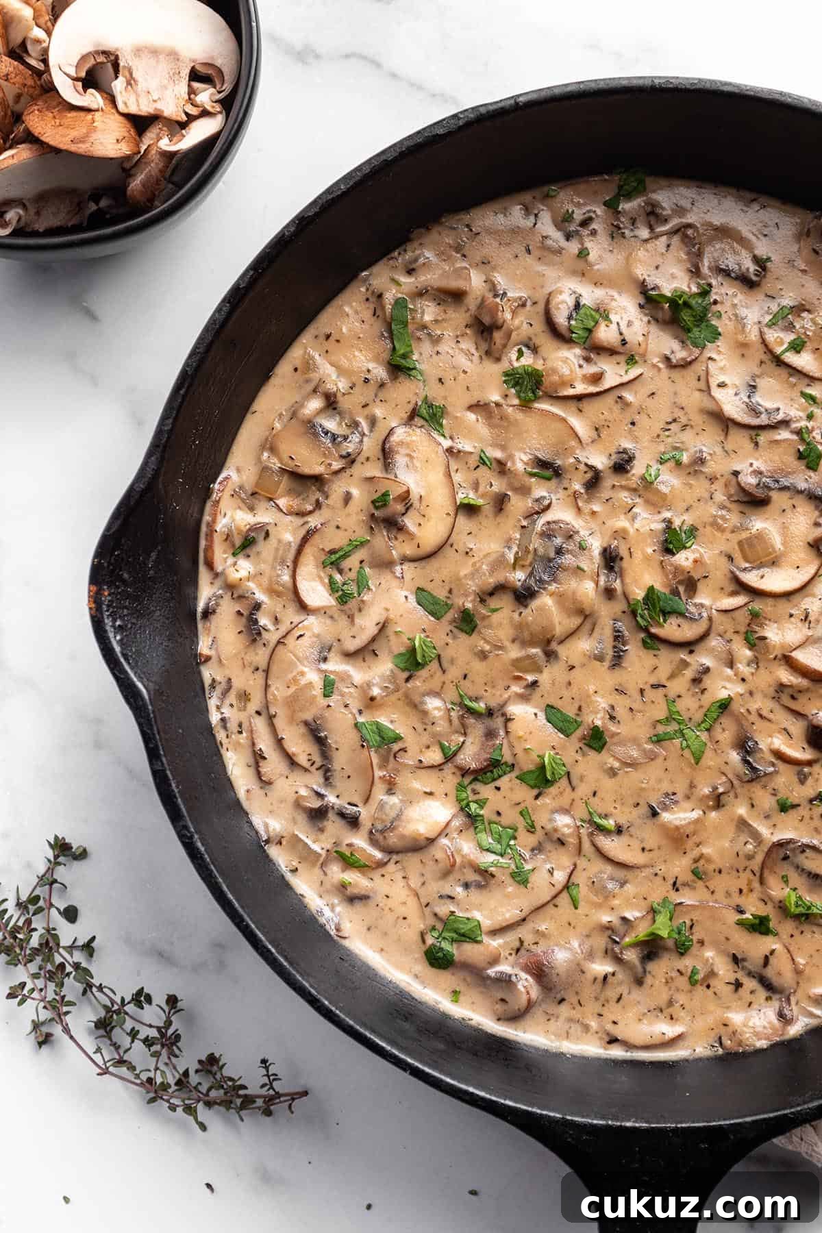 A cast iron skillet with a mushroom sauce and fresh parsley on top.