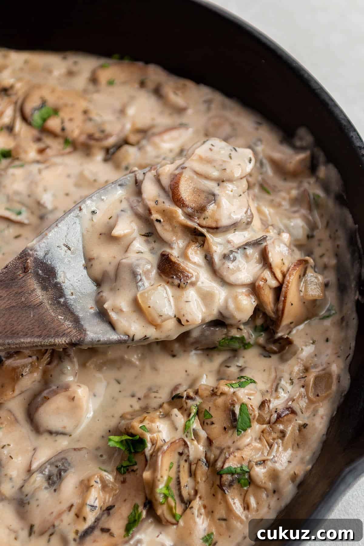 A cast iron skillet with a mushroom sauce and a wooden spoon scooping some out.