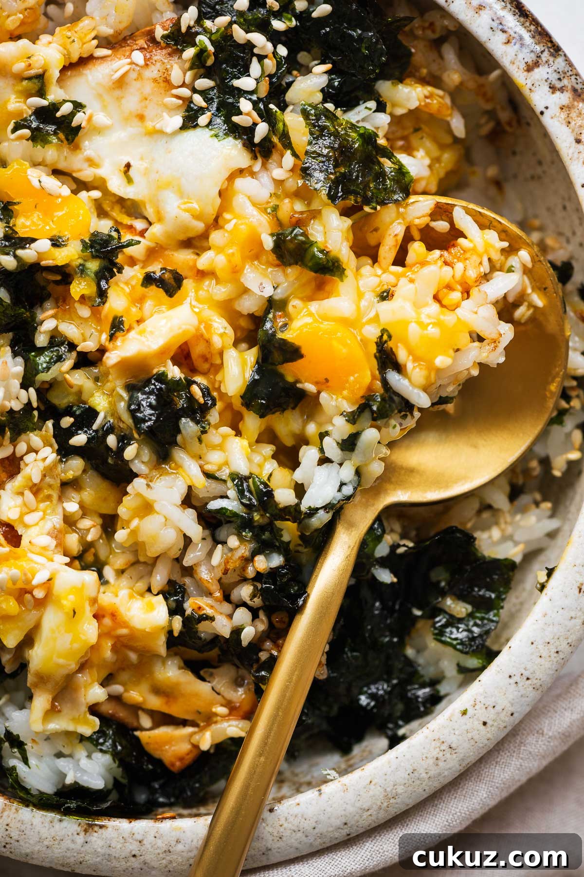 A close-up of a bowl of Korean egg rice with everything mixed together. The runny egg yolk creates a glossy sauce with the soy sauce, butter, and sesame oil to coat the rice kernels.