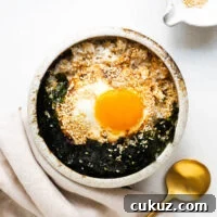 A ceramic bowl with fried rice, fried egg with a runny yolk, crushed seaweed and toasted sesame seeds, drizzled with soy sauce, sesame sauce and brown butter.