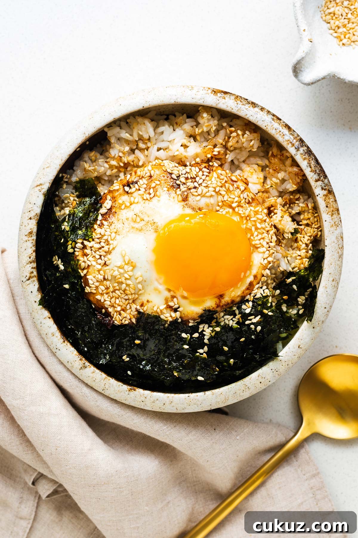 A soy sauce fried egg on rice with crushed gim (roasted seaweed) and sesame seeds in a ceramic bowl.