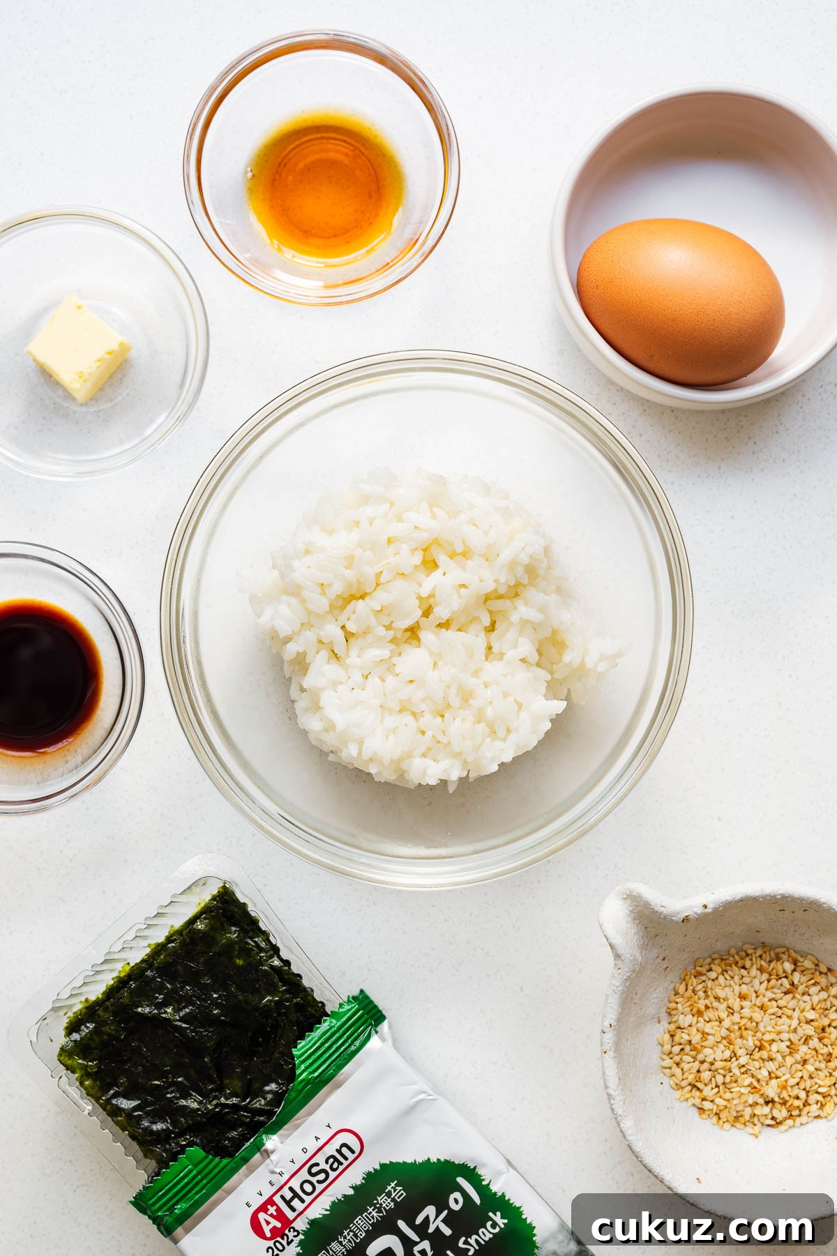 The simple ingredients you need for this gyeran bap recipe including cooked white rice, an egg, unsalted butter, soy sauce, sesame oil, roasted seaweed and toasted sesame seeds.