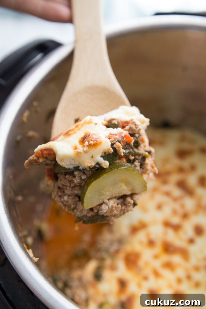 Wooden spoon with a bite of Instant Pot Zucchini Lasagna in the foreground, Instant Pot full of lasagna in the background.