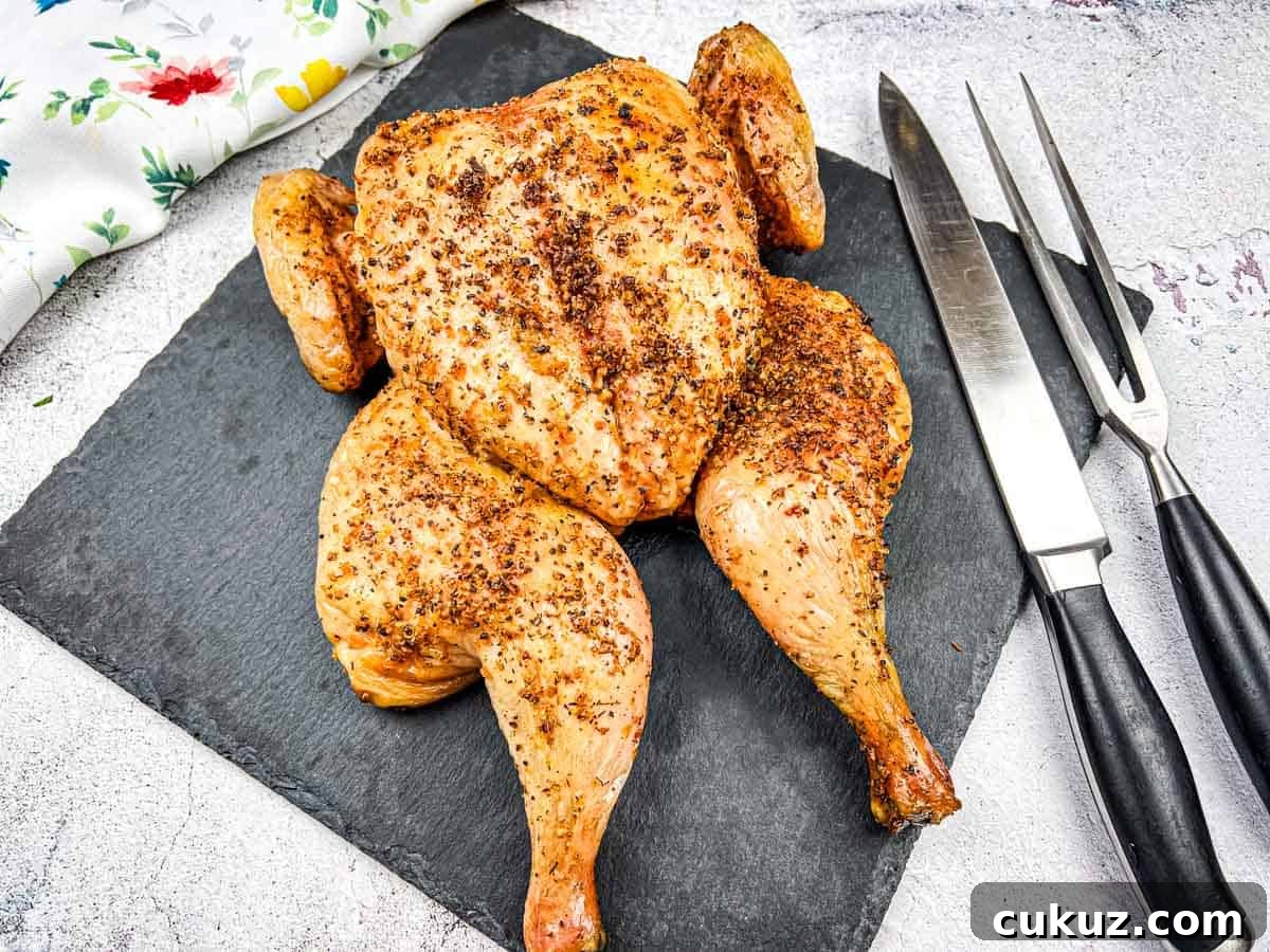 Roasted chicken on a slate board with carving knife and fork.