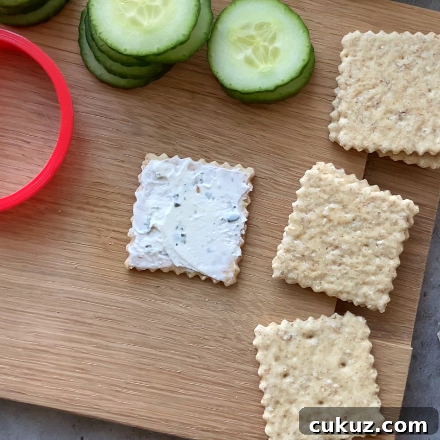 Square crackers on a wooden board, one topped with cream cheese.