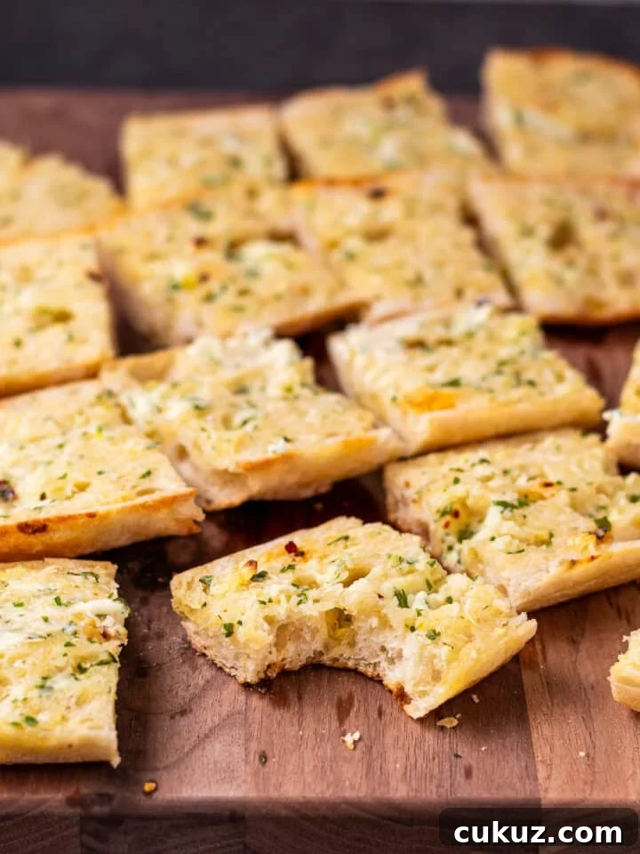 wood cutting board with pieces of buttery garlic bread. One piece has a bite taken out of it.