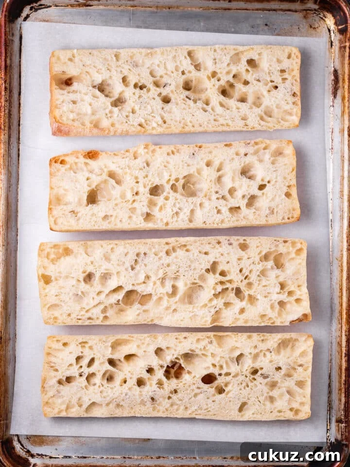 sliced ciabatta baguette on a lined sheet pan